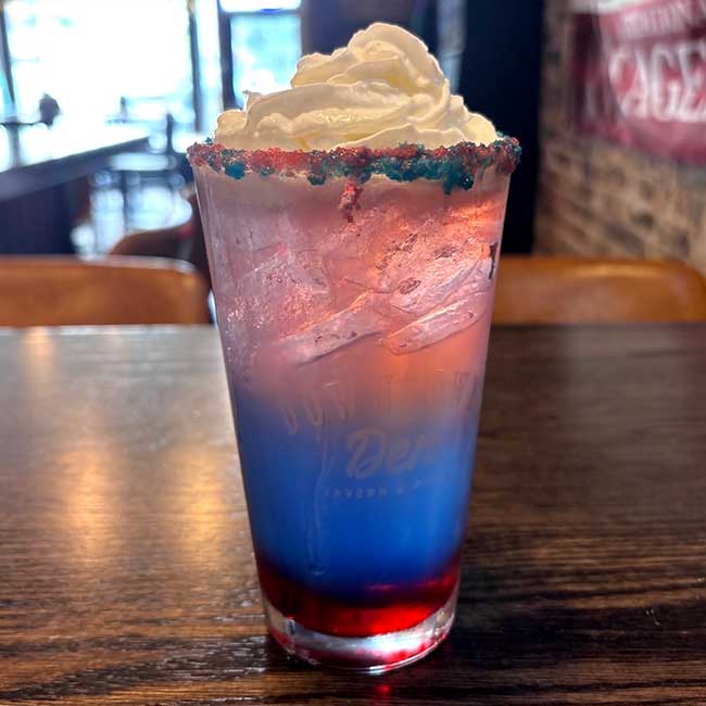 A layered red, white, and blue drink with whipped cream at a Beloit restaurant table.