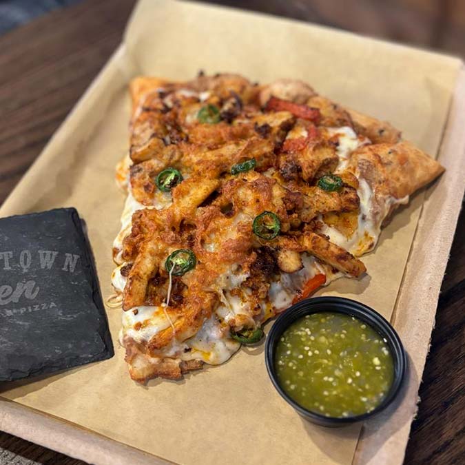 A slice of Pizza Beloit topped with chicken, jalapeños, and green salsa from Downtown Den.